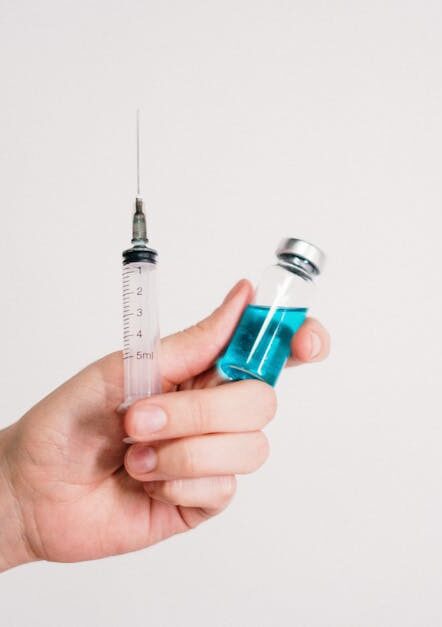 Hand holding a syringe and vaccine vial on a white background, symbolizing healthcare and immunization.